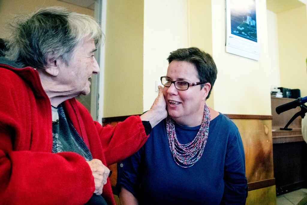 Seniorka hladí po tváři smějící se ženu v brýlích.